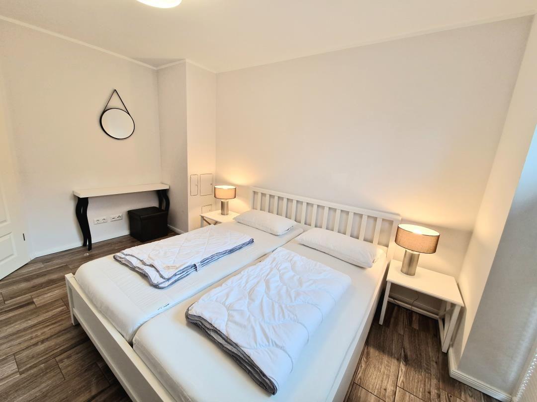Schlafzimmer mit Doppelbett, zwei Nachttischen und Lampen. Holzboden und Wandspiegel.
