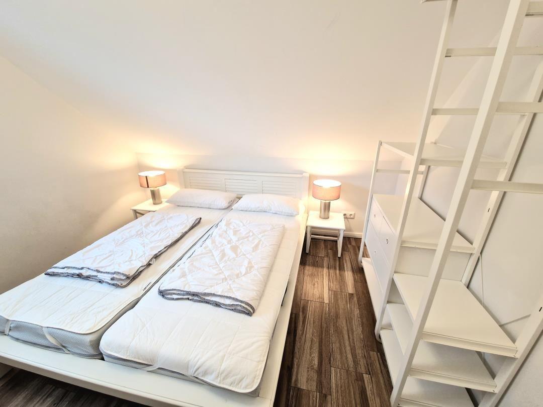 Schlafzimmer mit Doppelbett, zwei Nachttischen und einer Leiter zur Dachgeschosswohnung.