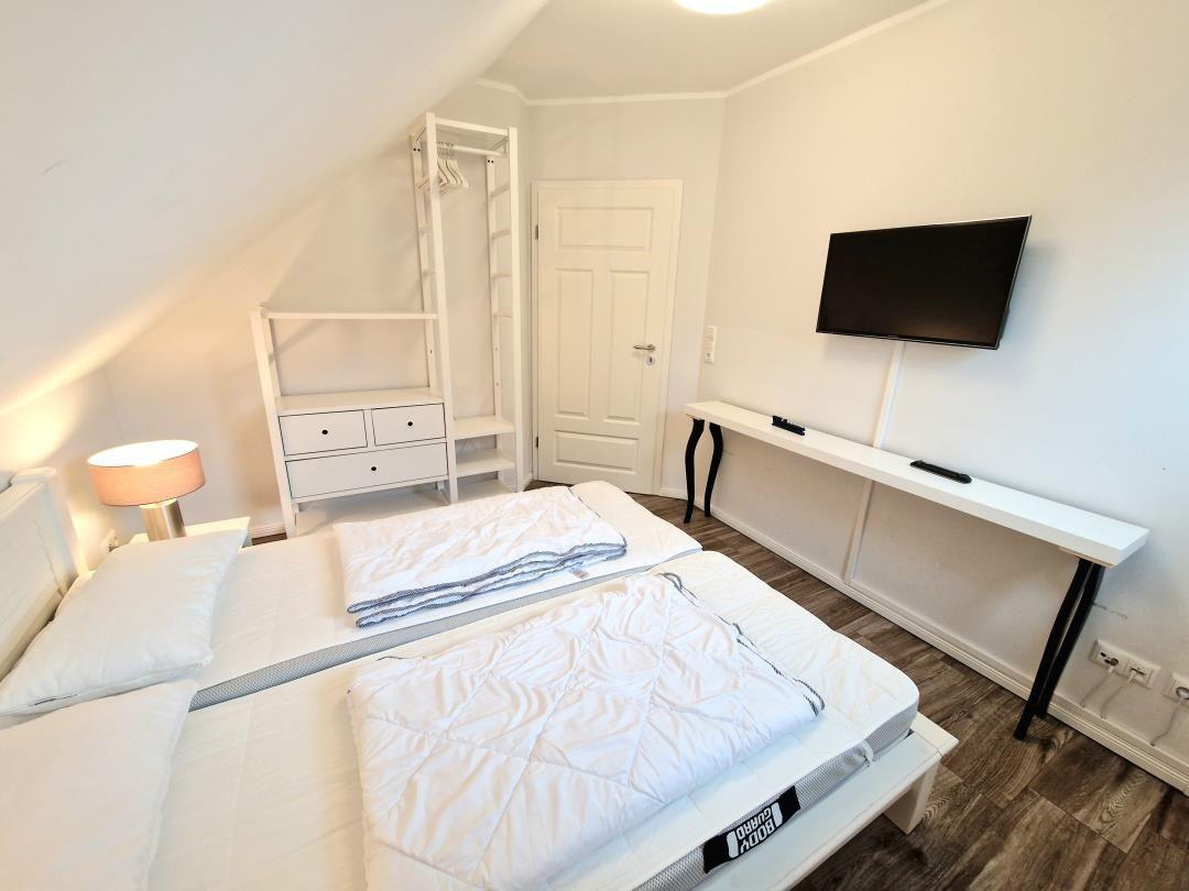 Schlafzimmer mit Doppelbett, Kleiderschrank, Schreibtisch und Wand-TV.