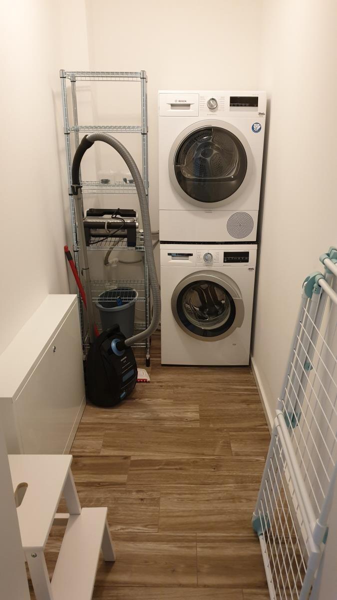 Waschmaschine und Trockner in einem kleinen Raum mit Holzboden und Metallregal.