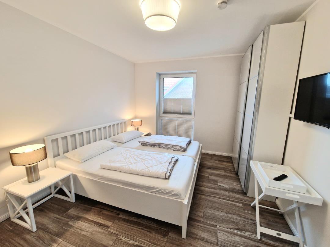 Schlafzimmer mit Doppelbett, Kleiderschrank und Fernseher an der Wand.