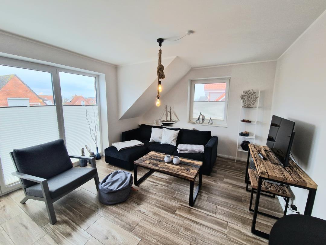 Wohnzimmer mit Sofa, Couchtisch und Schreibtisch. Große Fenster und Holzboden.