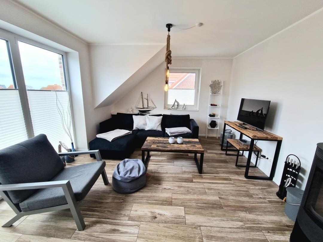 Wohnzimmer mit Sofa, Couchtisch und Fernseher. Holzboden und große Fenster.