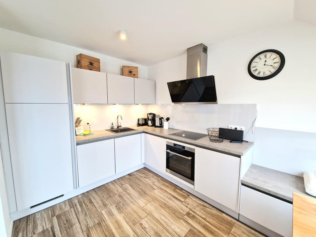 Moderne Küche mit weißen Schränken, Edelstahlgeräten und Holzboden.