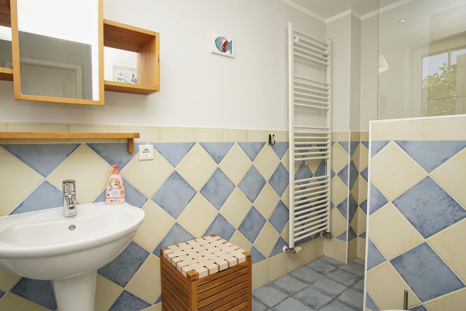 Badezimmer mit Waschbecken, Spiegel, Heizkörper und gefliesten Wänden.