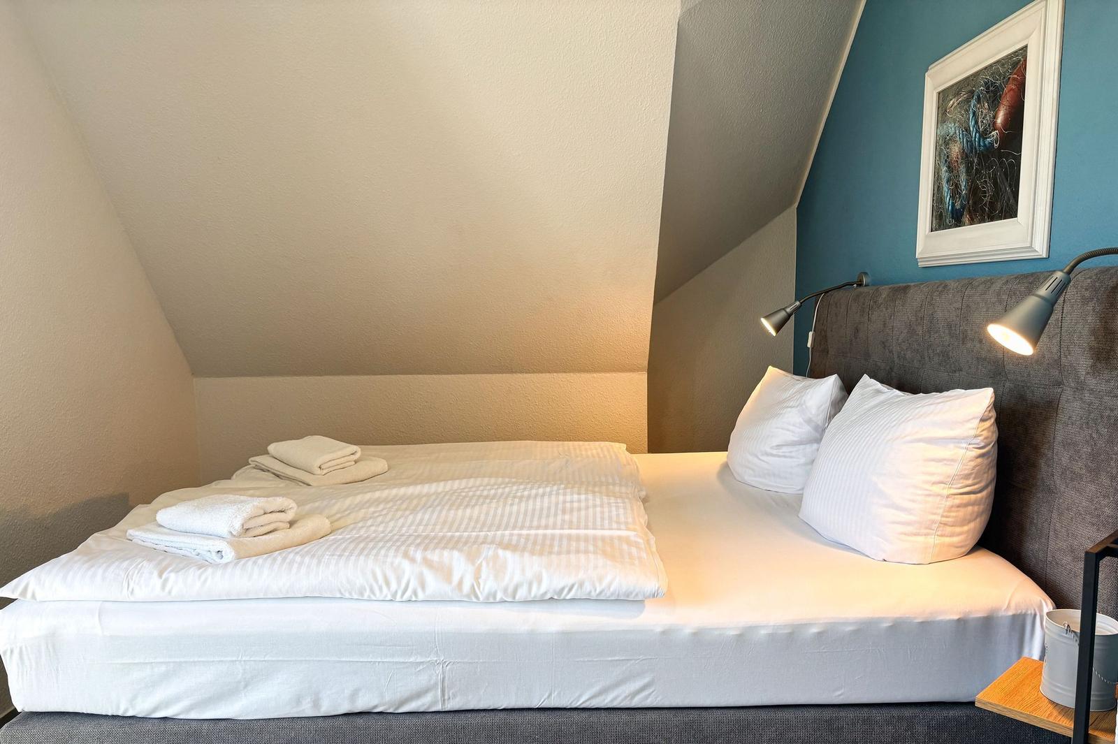 Schlafzimmer mit Doppelbett, weißen Bettwäsche und zwei Nachttischlampen an grauem Kopfteil.