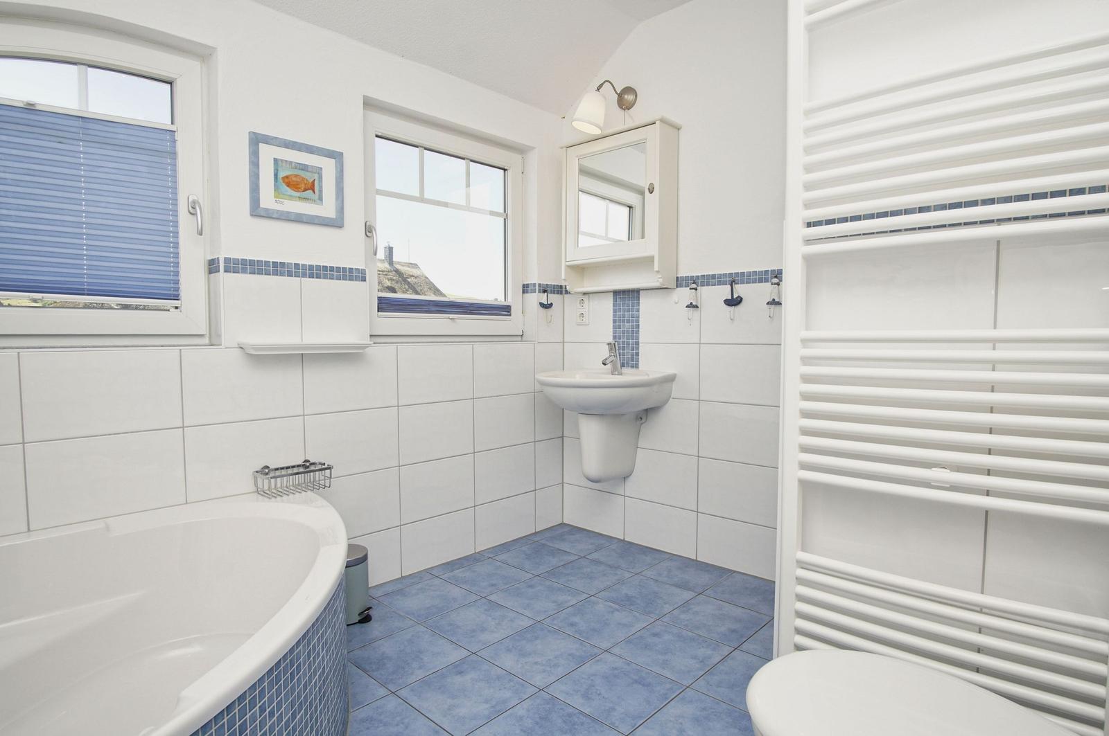 Badezimmer mit Badewanne, Waschbecken und Heizung. Fenster mit Jalousie und Wandbild.