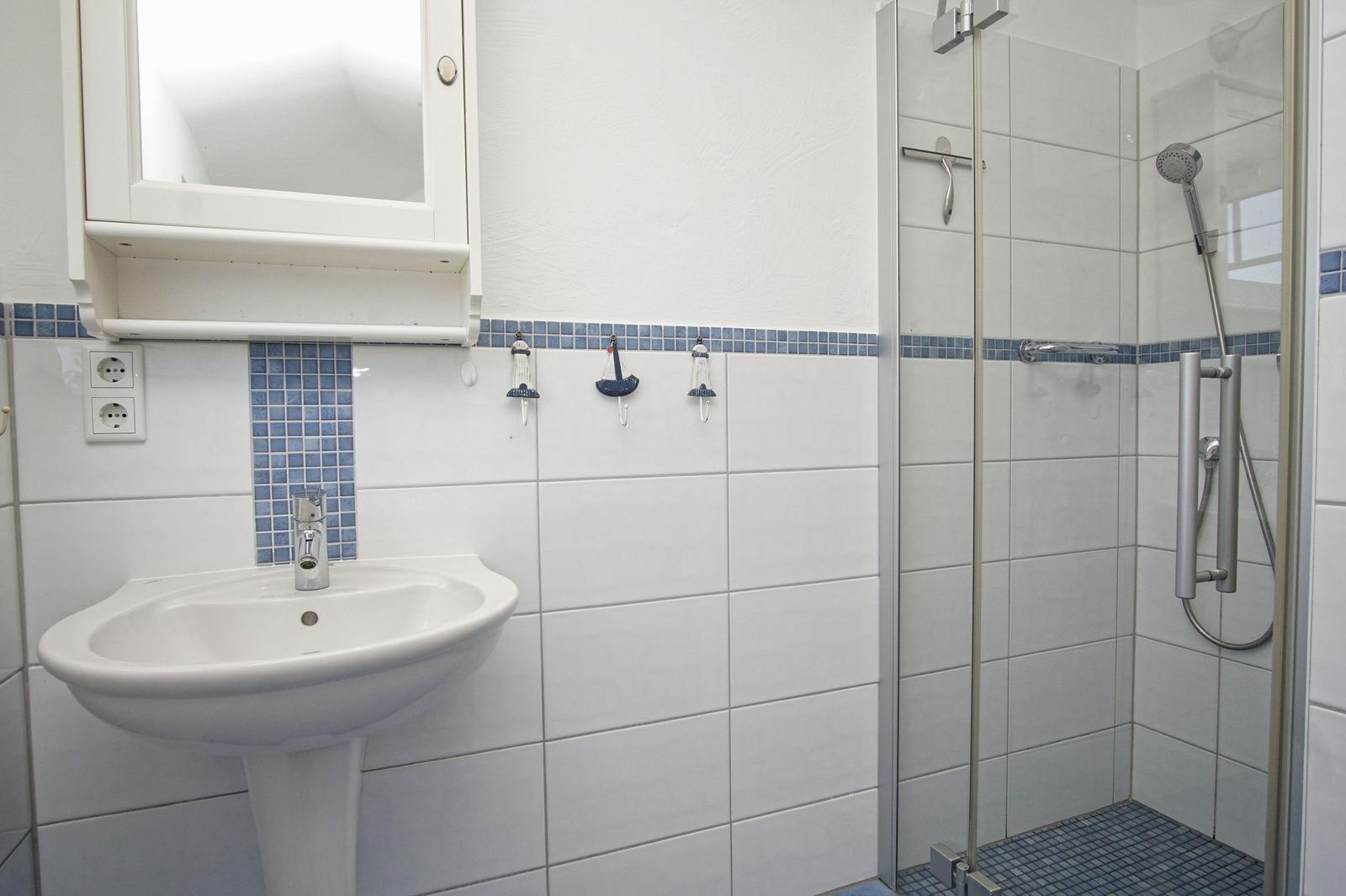 Badezimmer mit Dusche, Waschbecken und Spiegelschrank. Wandverkleidung mit blauen Fliesen.