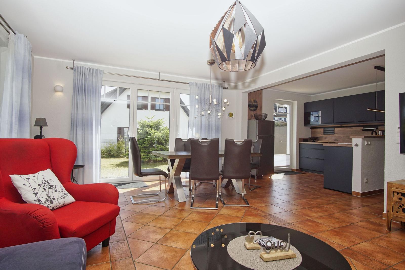 Wohn- und Essbereich mit rotem Sofa, Esstisch und Küche im Hintergrund.