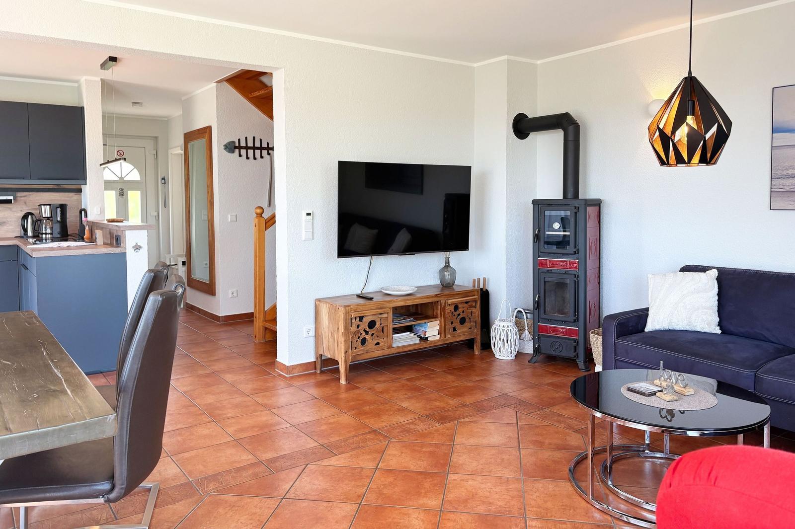 Wohnzimmer mit Sofa, TV und Holz-TV-Tisch. Kaminofen und Esstisch im Hintergrund.