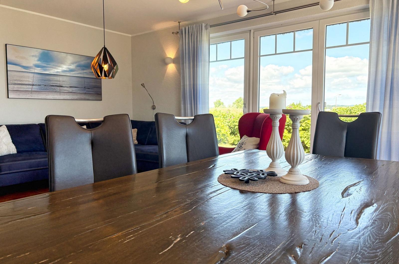 Esszimmer mit Holztisch, Stühlen und Blick auf Grün. Wandbild und Pendelleuchte sichtbar.