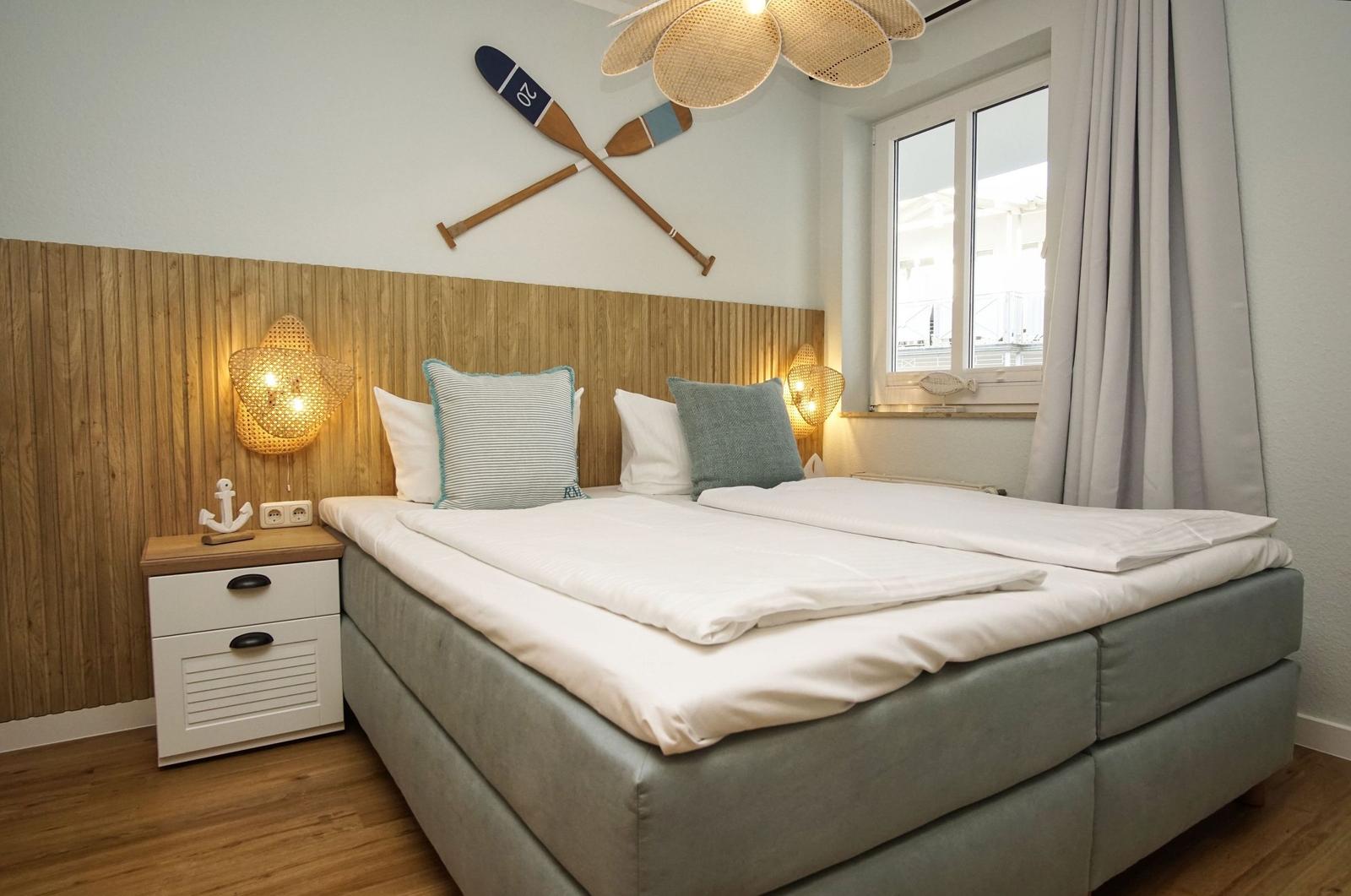 Schlafzimmer mit Bett, Nachttisch und Fenster. Wanddekoration mit Ruder und Lampen.