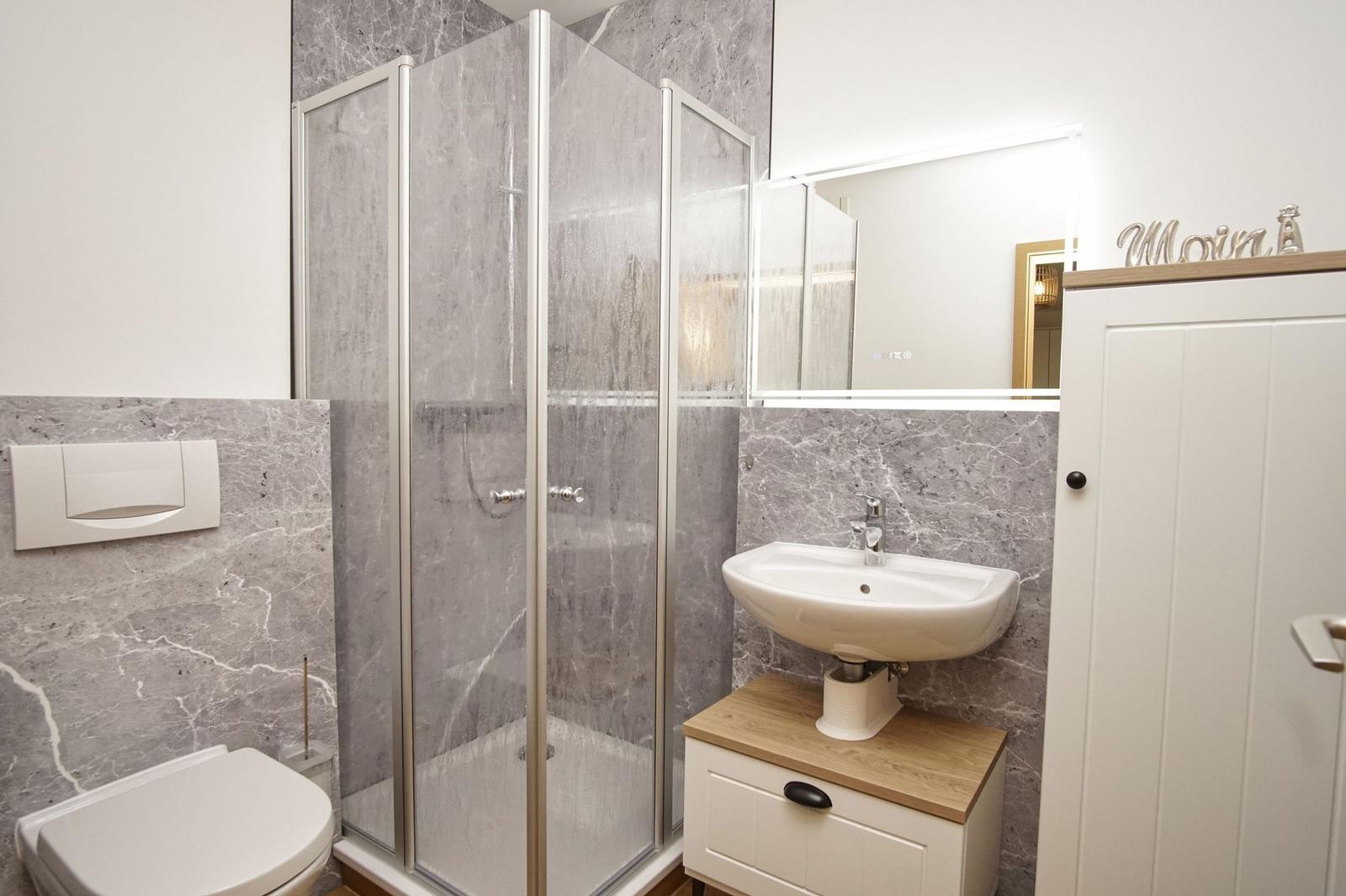 Badezimmer mit Dusche, Waschbecken und Toilette. Wandverkleidung aus grauem Marmor.