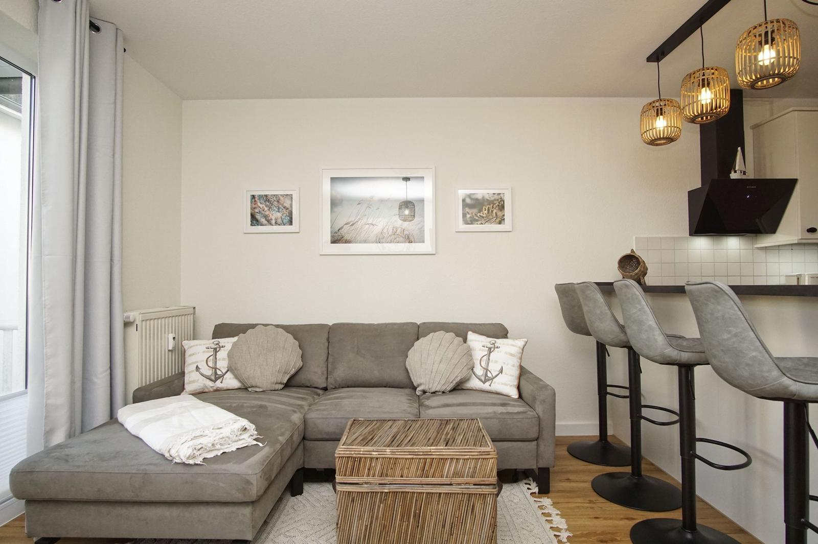 Wohnbereich mit Sofa, Kissen und Esstisch. Küchenzeile mit Barhocker.
