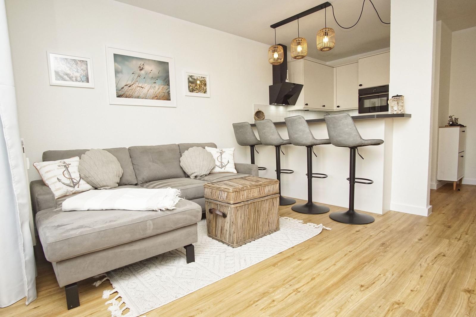 Wohnbereich mit Sofa, Barhocker und Küchenzeile. Holzboden und Wandbilder.