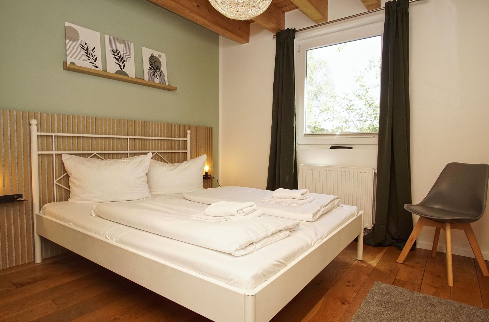Bedroom with white bed, wooden floor, and window with green curtains.