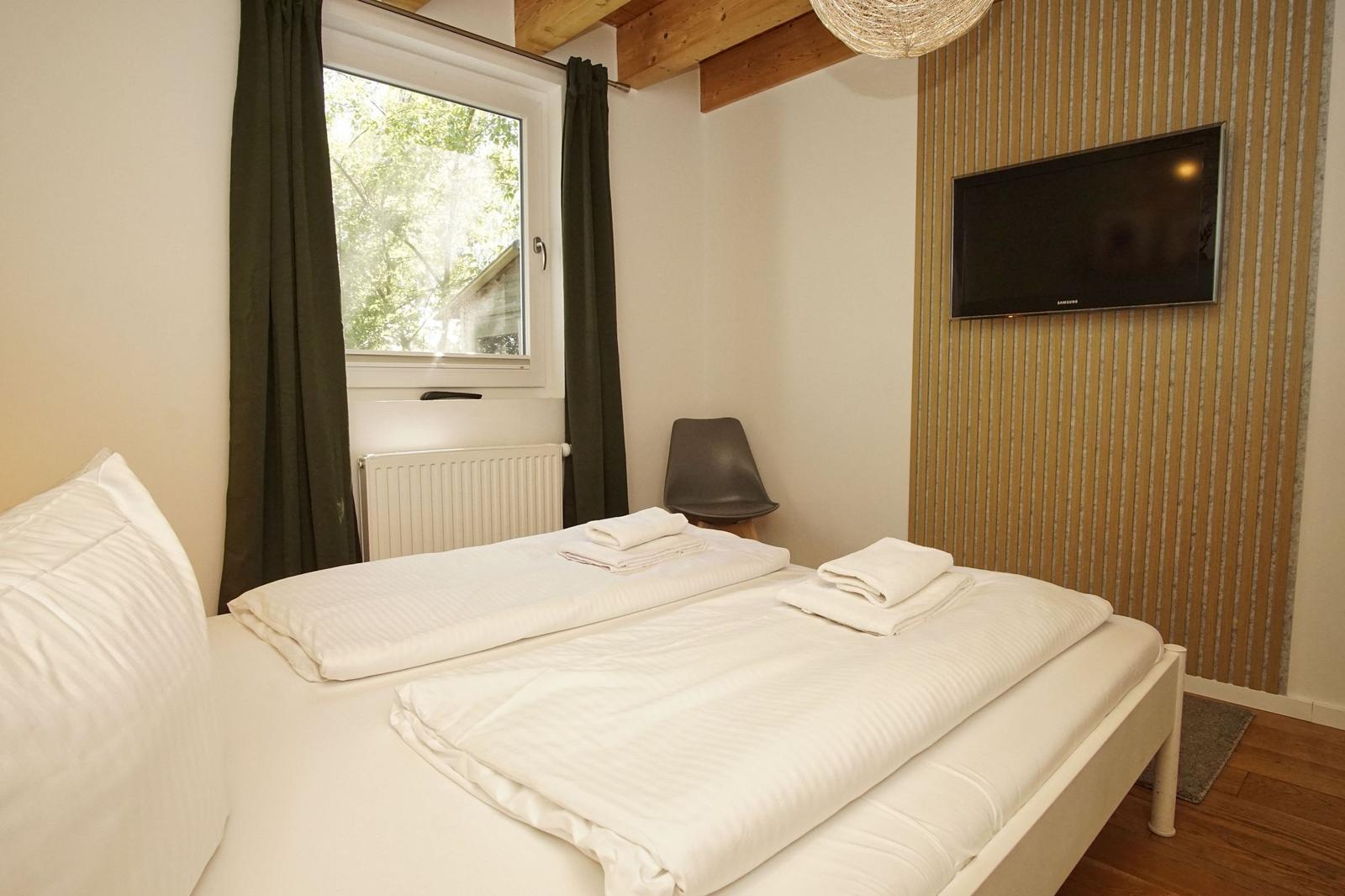 A bedroom with bed, window, TV, and chair.