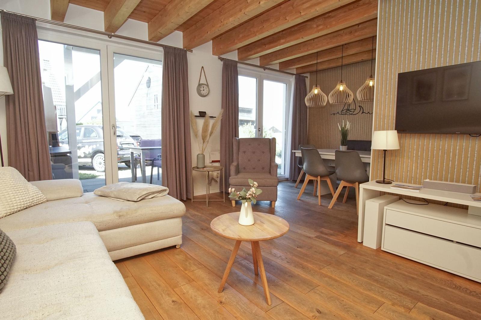 Living room with wooden floor, sofa, armchair, and dining area. Wooden ceiling and large windows.