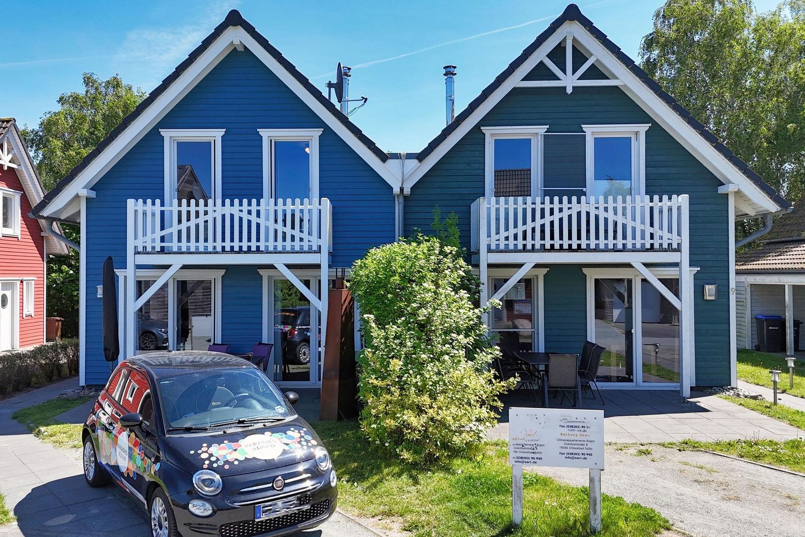 Two vacation homes with balconies and terraces. A car is parked in front.