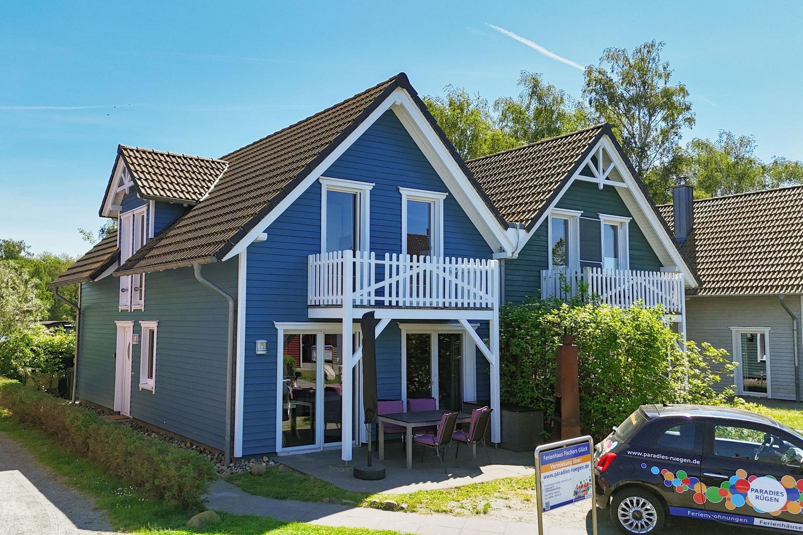 Holiday home with blue and green wood siding, white balconies, and terrace with table and chairs.