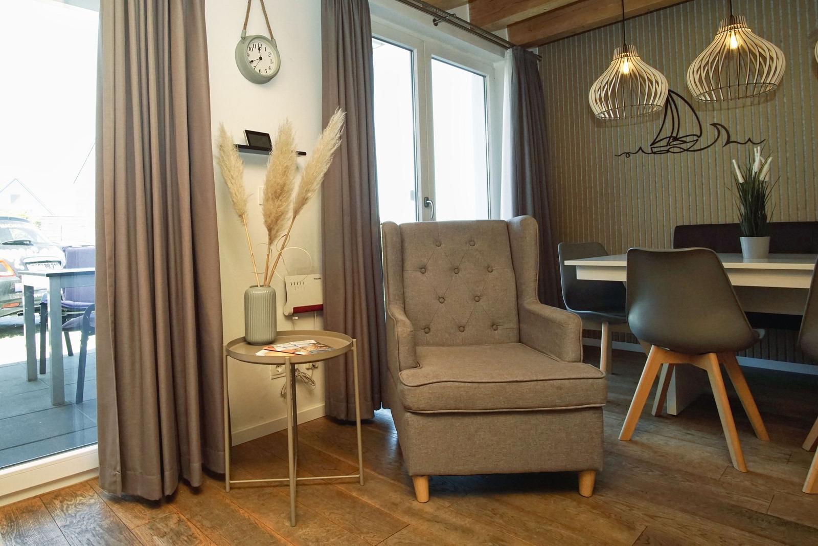 An armchair stands next to a table with pampas grass. In the background is a dining area with table and chairs.
