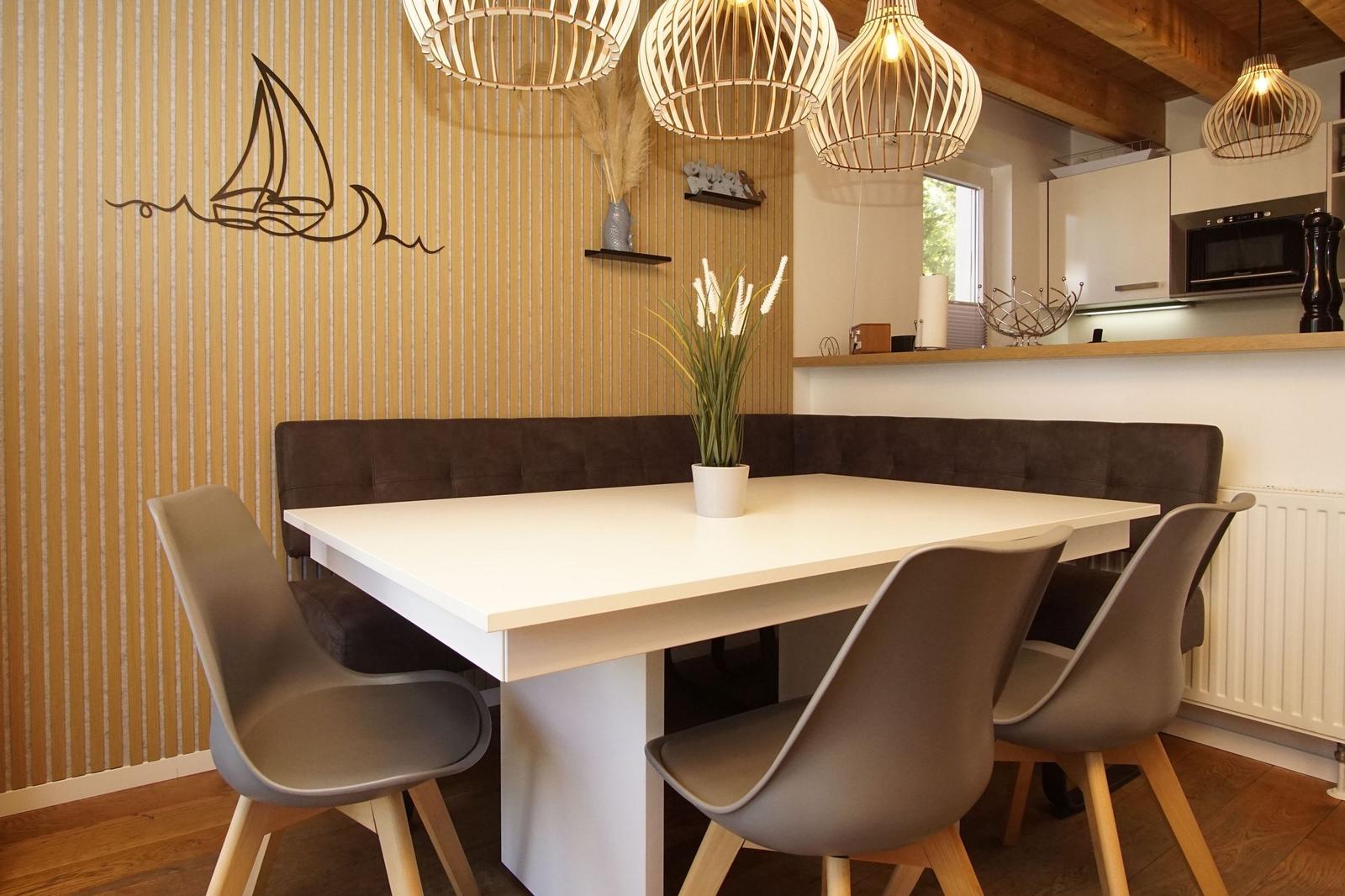 Dining table with bench and chairs, wall with sailboat motif and pendant lights.