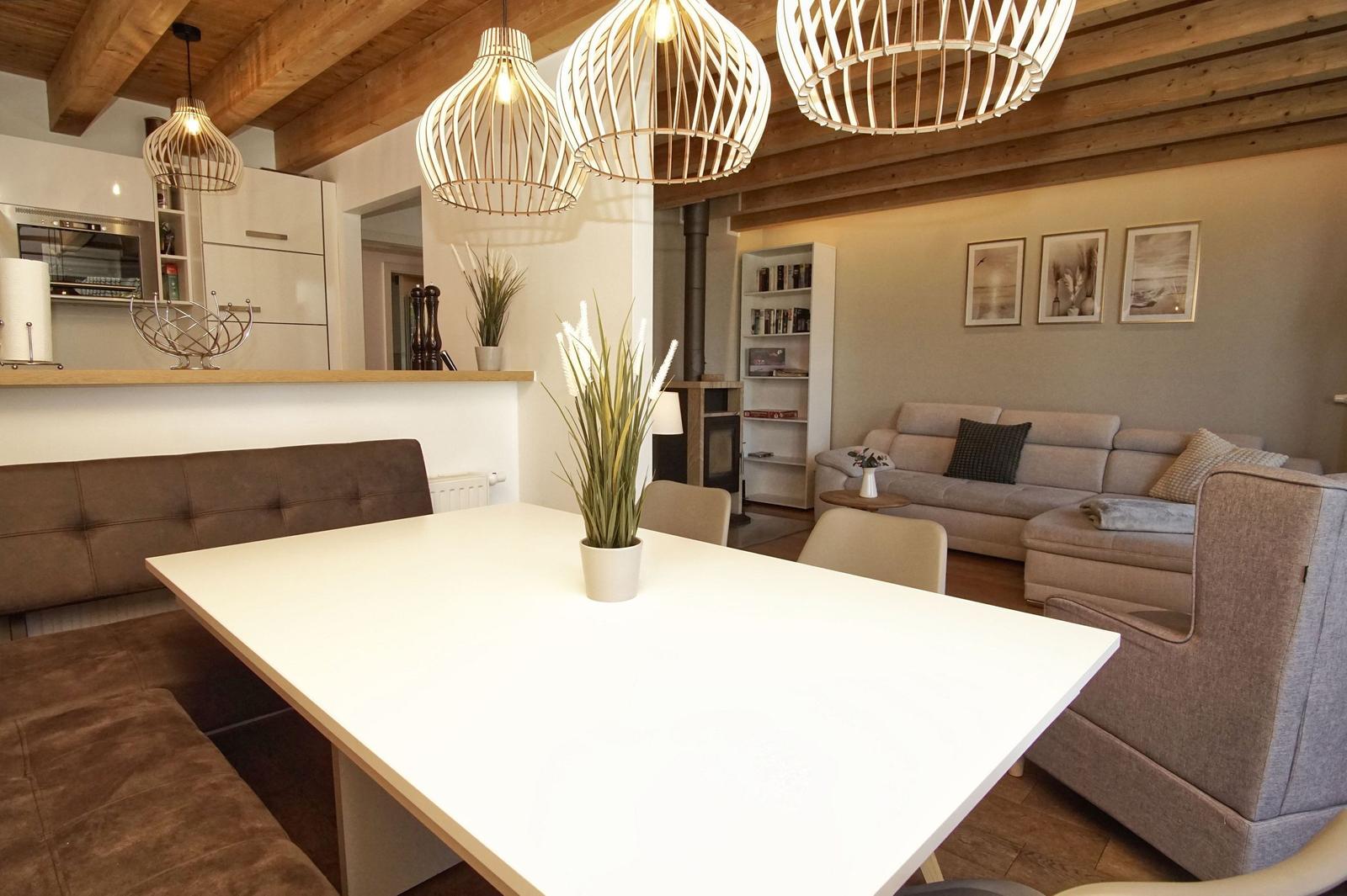 Dining area with table and bench, living area with sofa and bookcase under wooden beam ceiling.