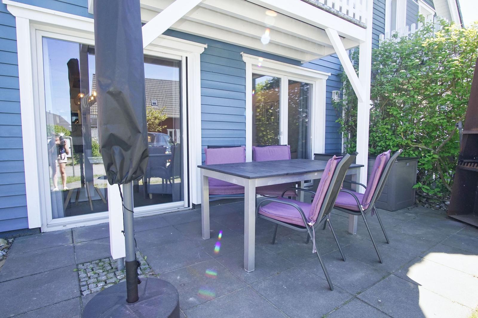 Terrace with table, chairs, and umbrella in front of blue house
