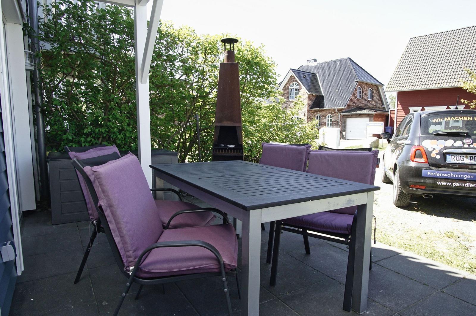 Terrace with table, chairs, and grill. Background: house and car.