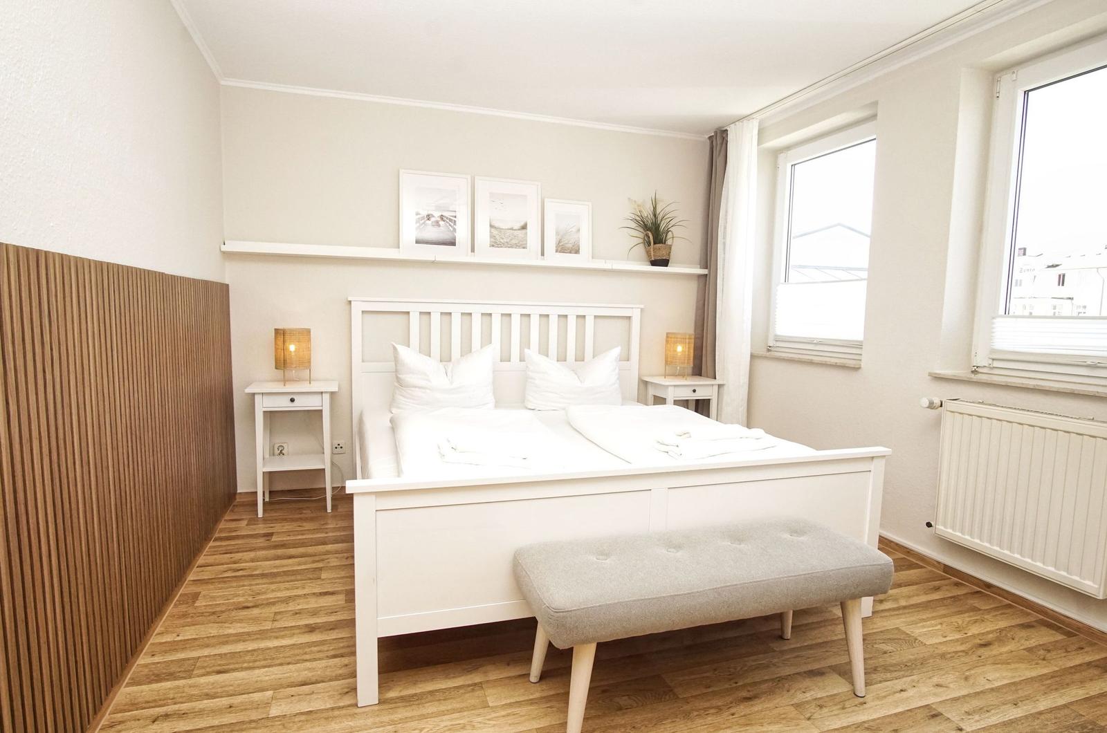 Ein Schlafzimmer mit weißem Bett, Holzboden und Fenstern.