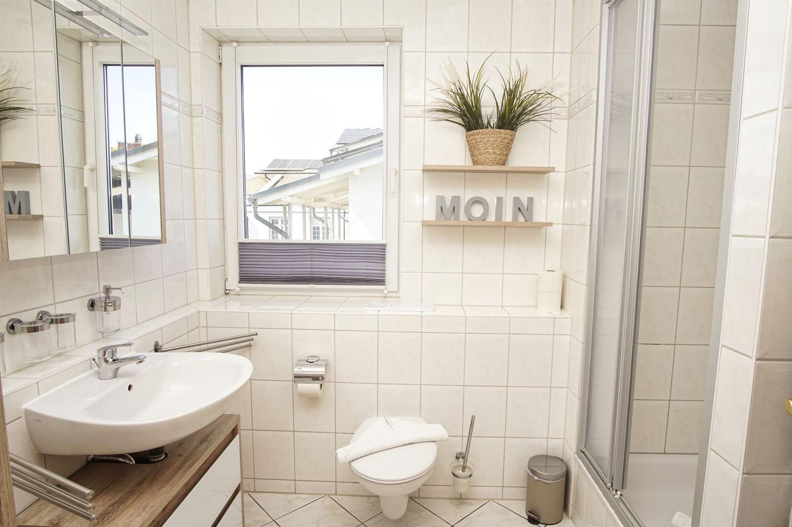 Badezimmer mit Waschbecken, Toilette und Dusche. Fenster mit Blick nach draußen.