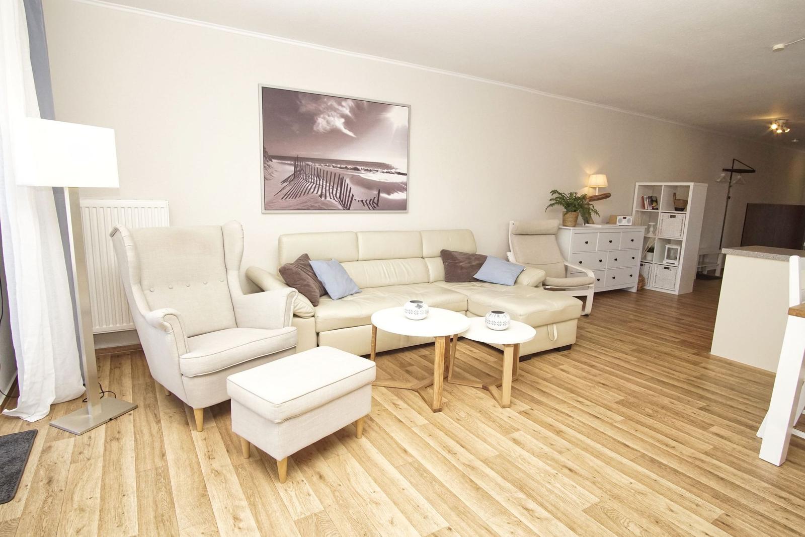 Wohnzimmer mit cremefarbenem Sofa, Sessel und Holzboden. Wandbild und Beistelltische.