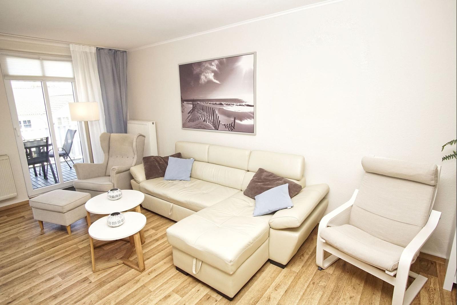 Wohnzimmer mit cremefarbenem Sofa, zwei Sesseln und einem Tisch. An der Wand hängt ein Bild.