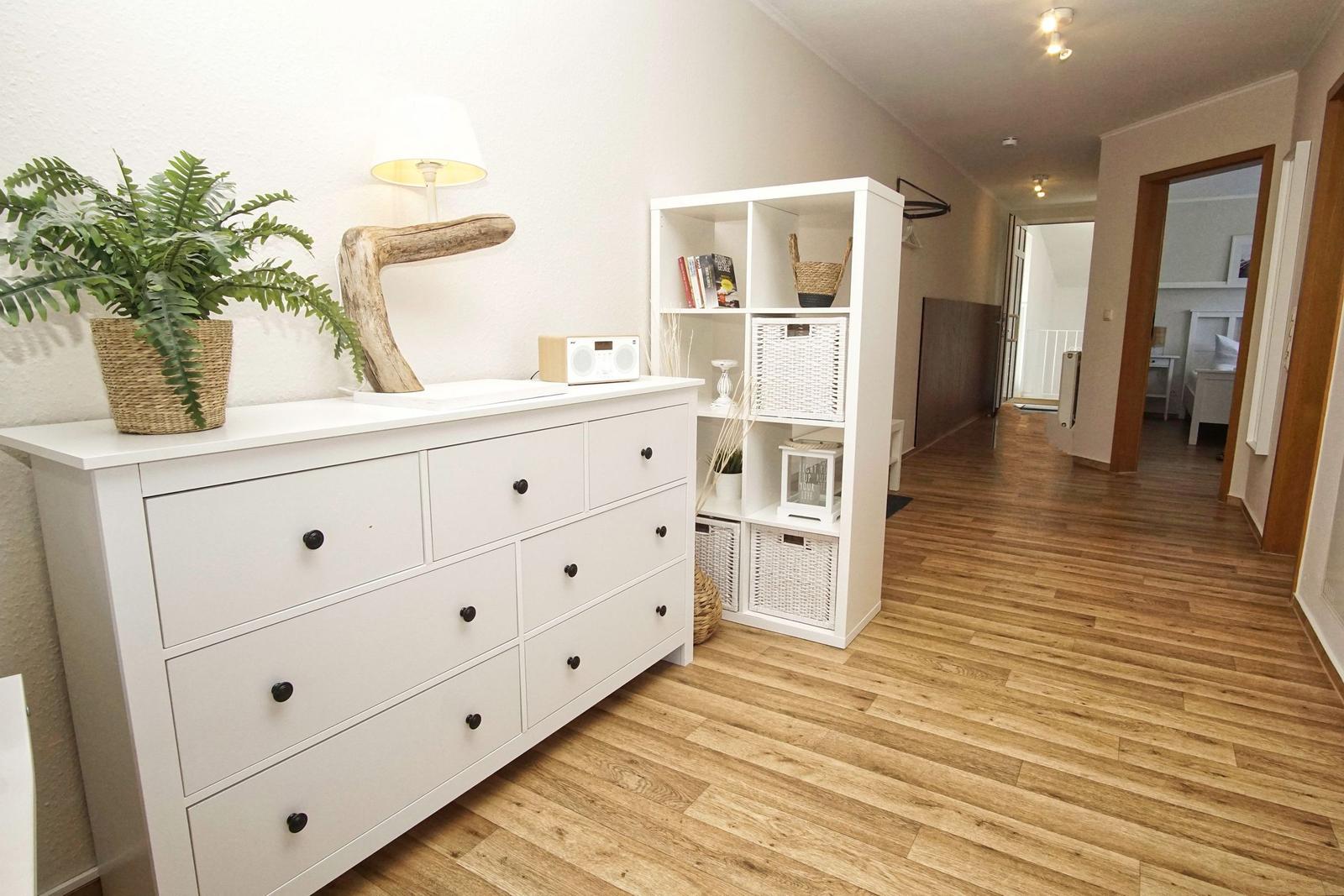Wohnbereich mit weißen Schränken, Pflanze und Holzboden. Durchgang zur Schlafzimmer.