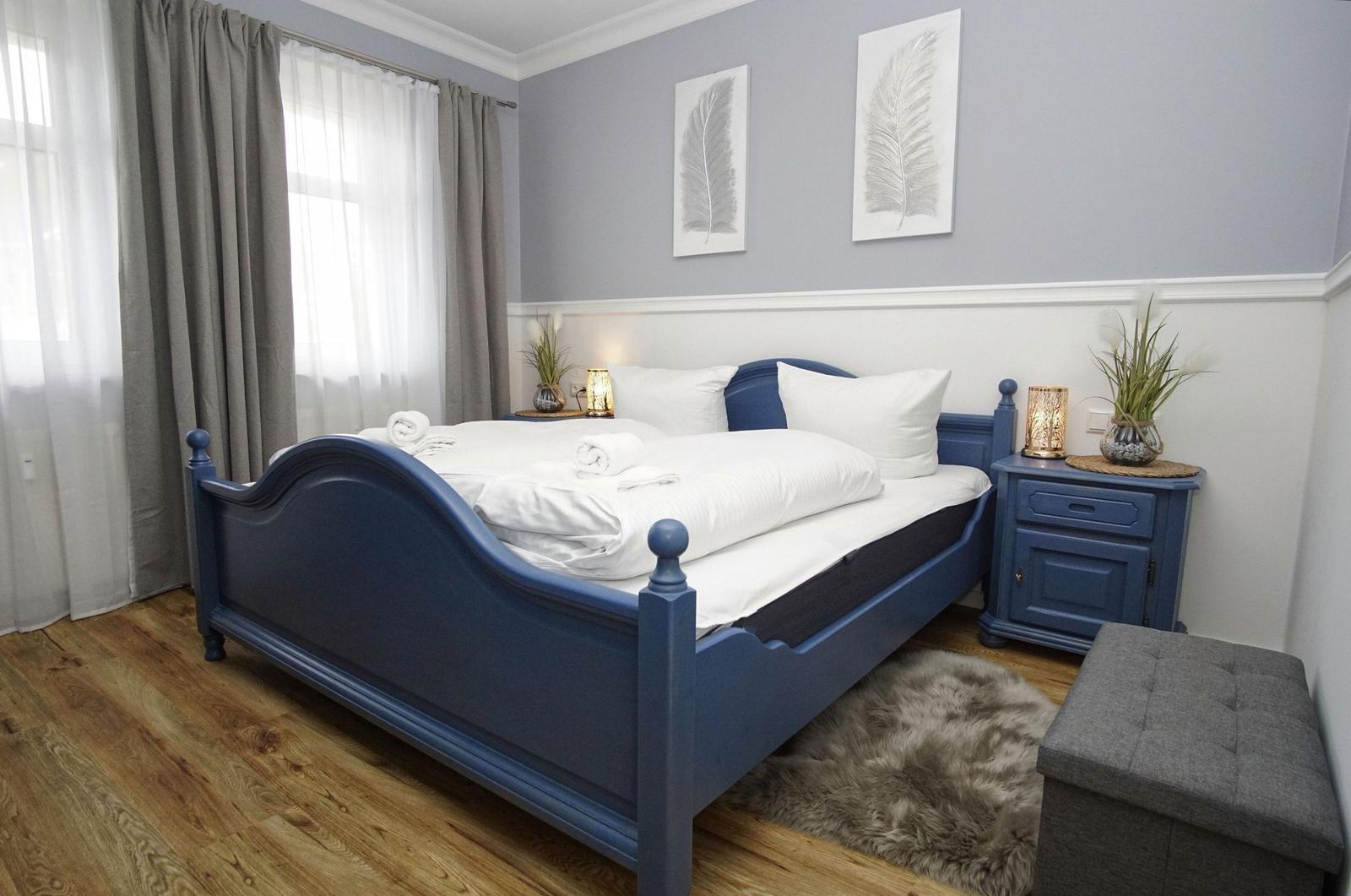 Bedroom with blue bed frame, white linens, and wooden floor.