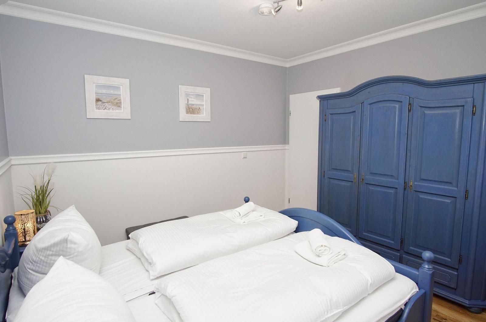 Bedroom with blue bed and wardrobe, white walls and pictures on the wall.