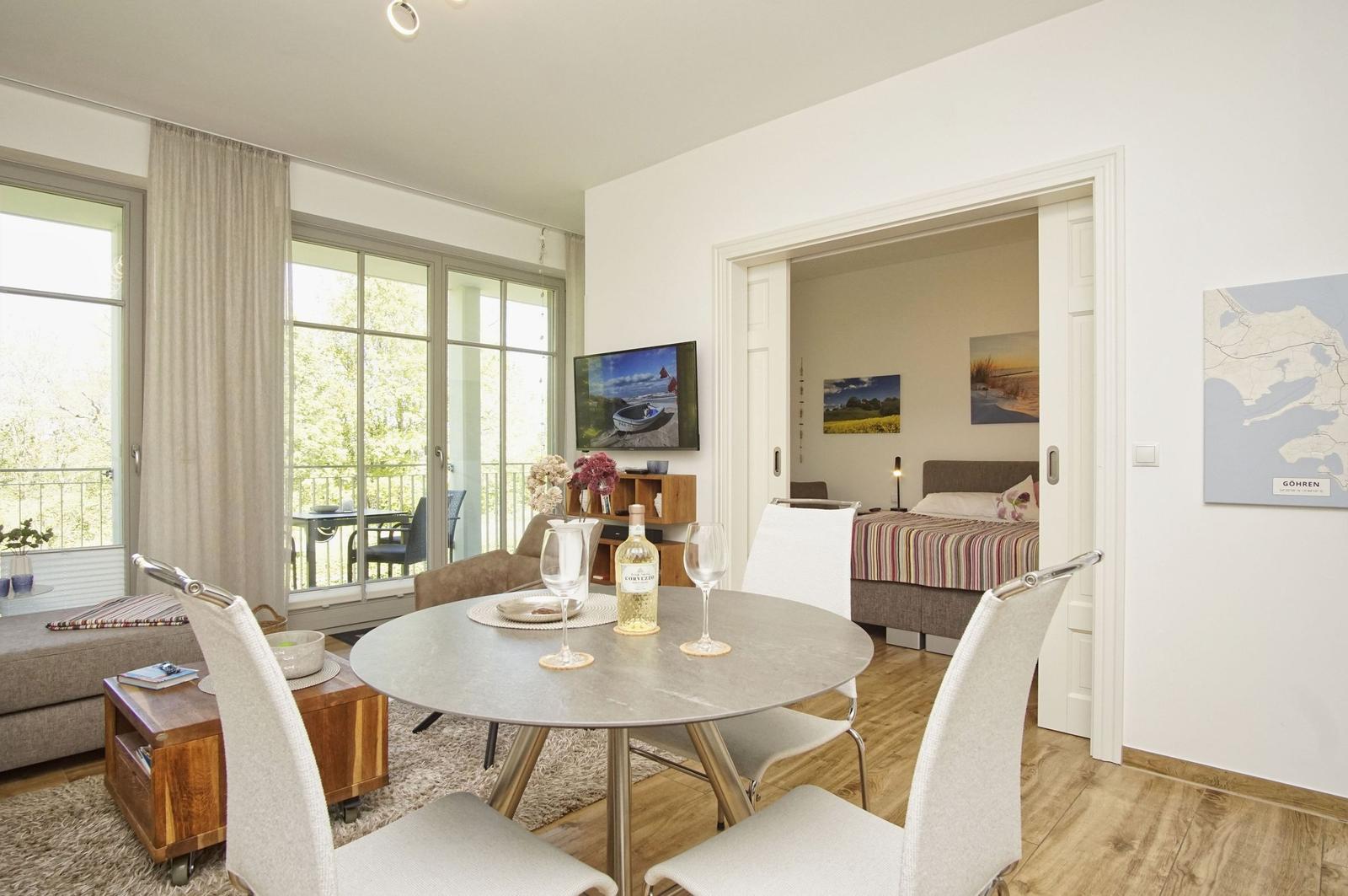 Wohnung mit Essbereich, Schlafzimmer und Balkon. Tisch mit Wein und Gläsern.