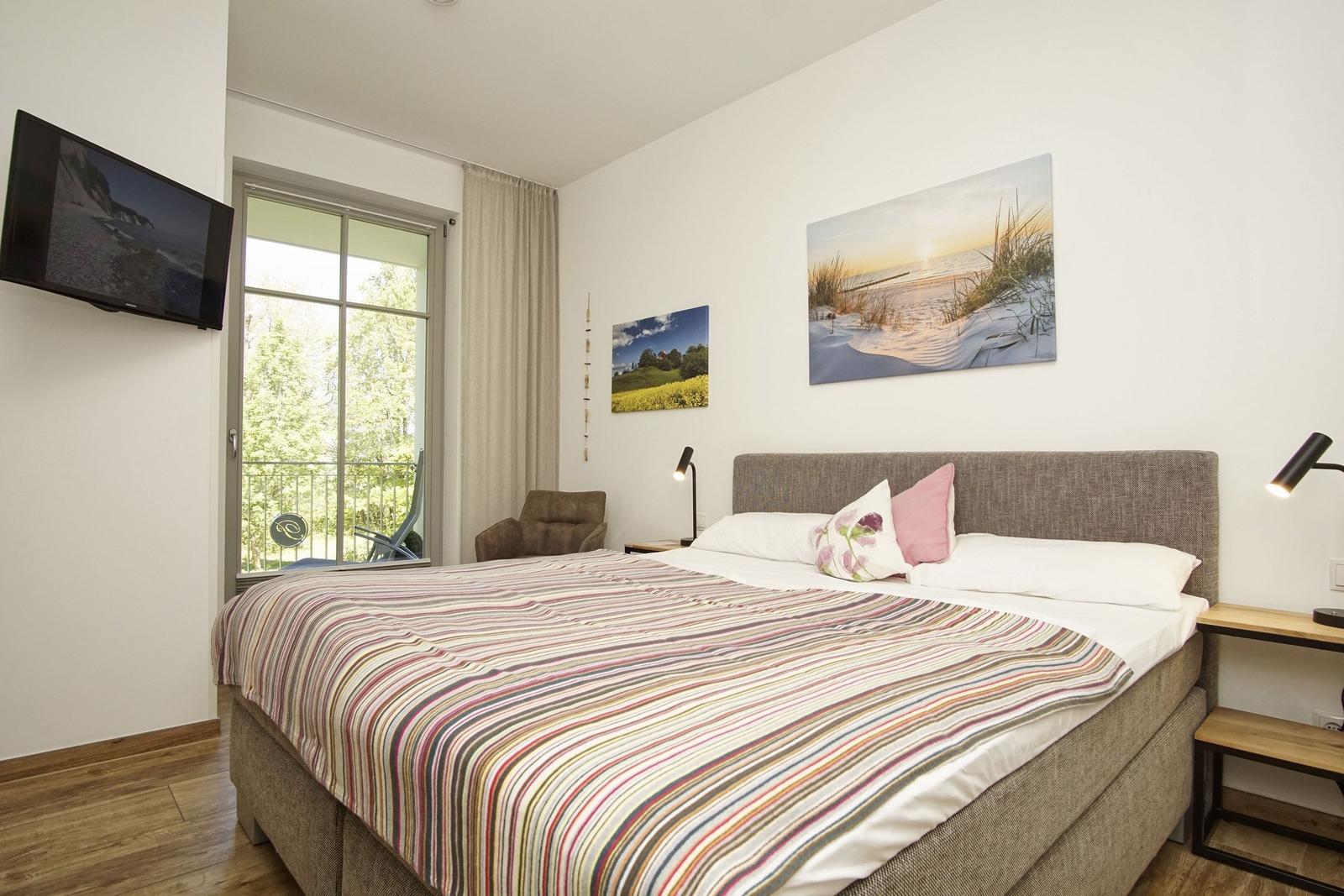 Schlafzimmer mit Bett, Fenster, TV und Wandbildern