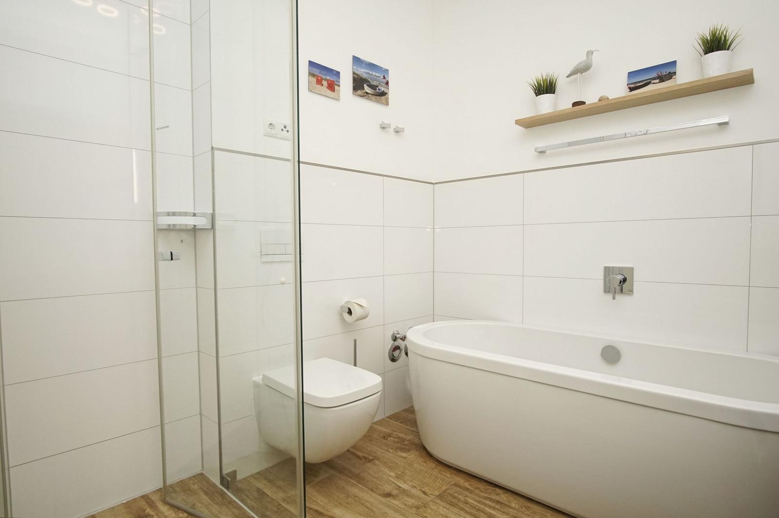 Badezimmer mit Dusche, Toilette und Badewanne. Holzfußboden und weiße Fliesen.