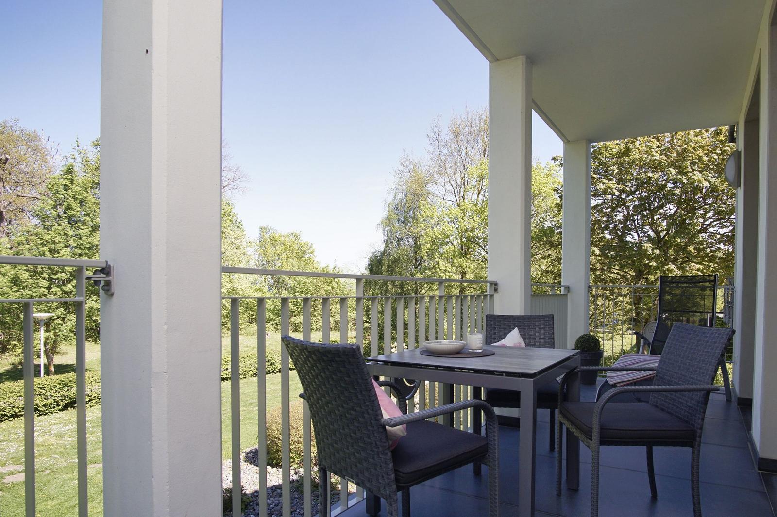 Terrasse mit Tisch und Stühlen, Blick auf grünen Garten und Bäume.