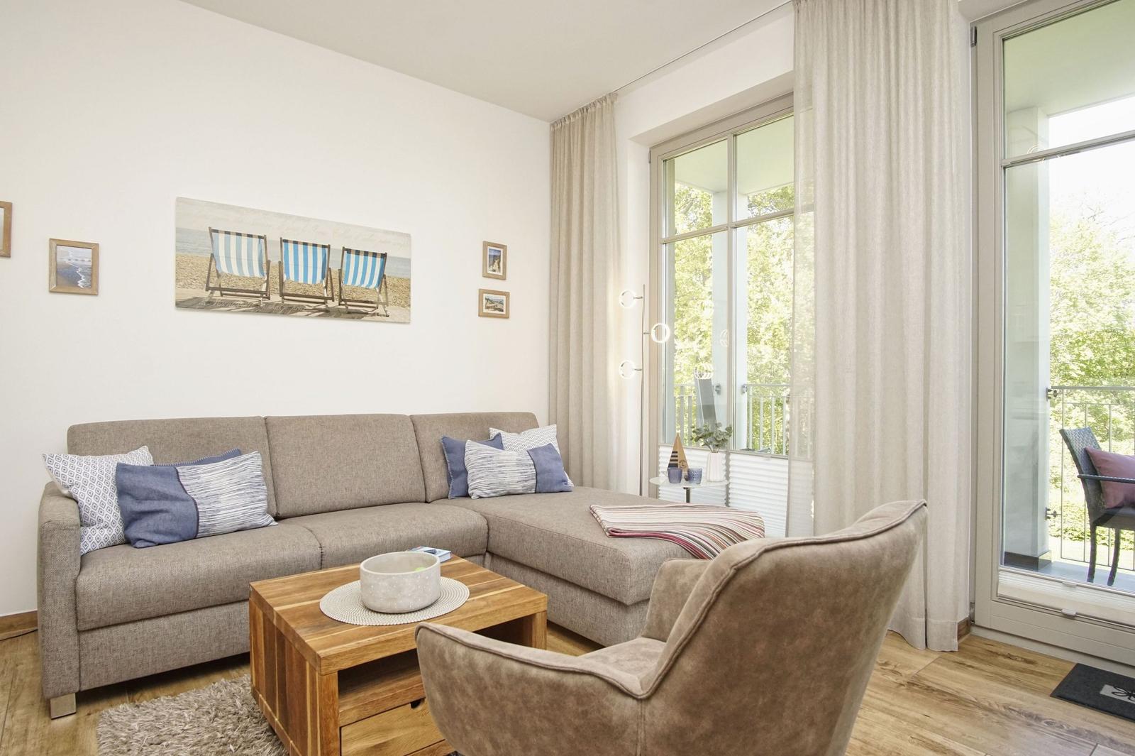 Wohnzimmer mit Sofa, Sessel und Balkonansicht. Wandbild mit Strandstühlen.