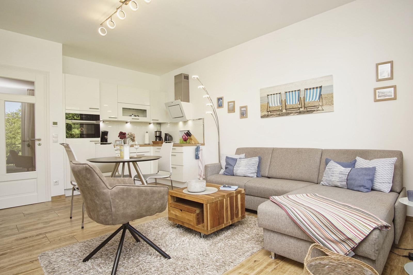 Wohnzimmer mit Sofa, Couchtisch und Küchenbereich. Wandbild mit Strandstühlen.