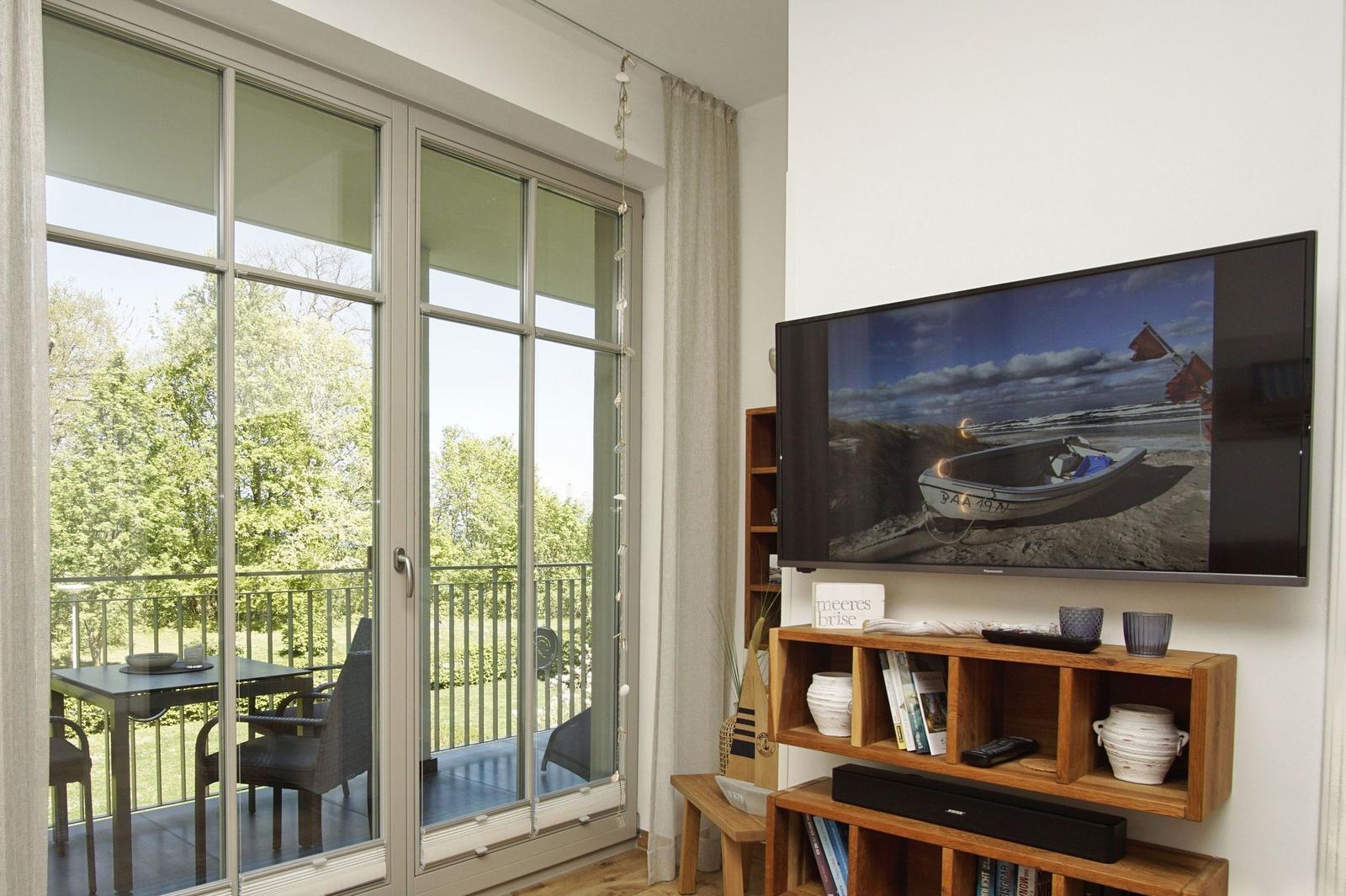 Wohnzimmer mit TV, Balkon und Blick auf Grün.