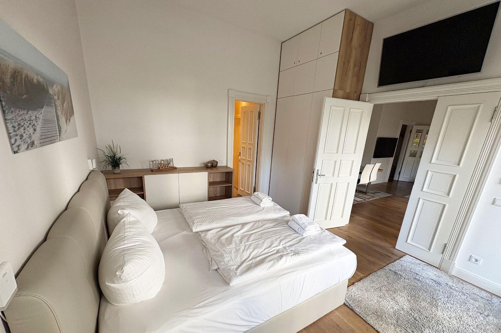 Schlafzimmer mit Doppelbett, Kleiderschrank und TV. Tür führt in Wohnbereich.