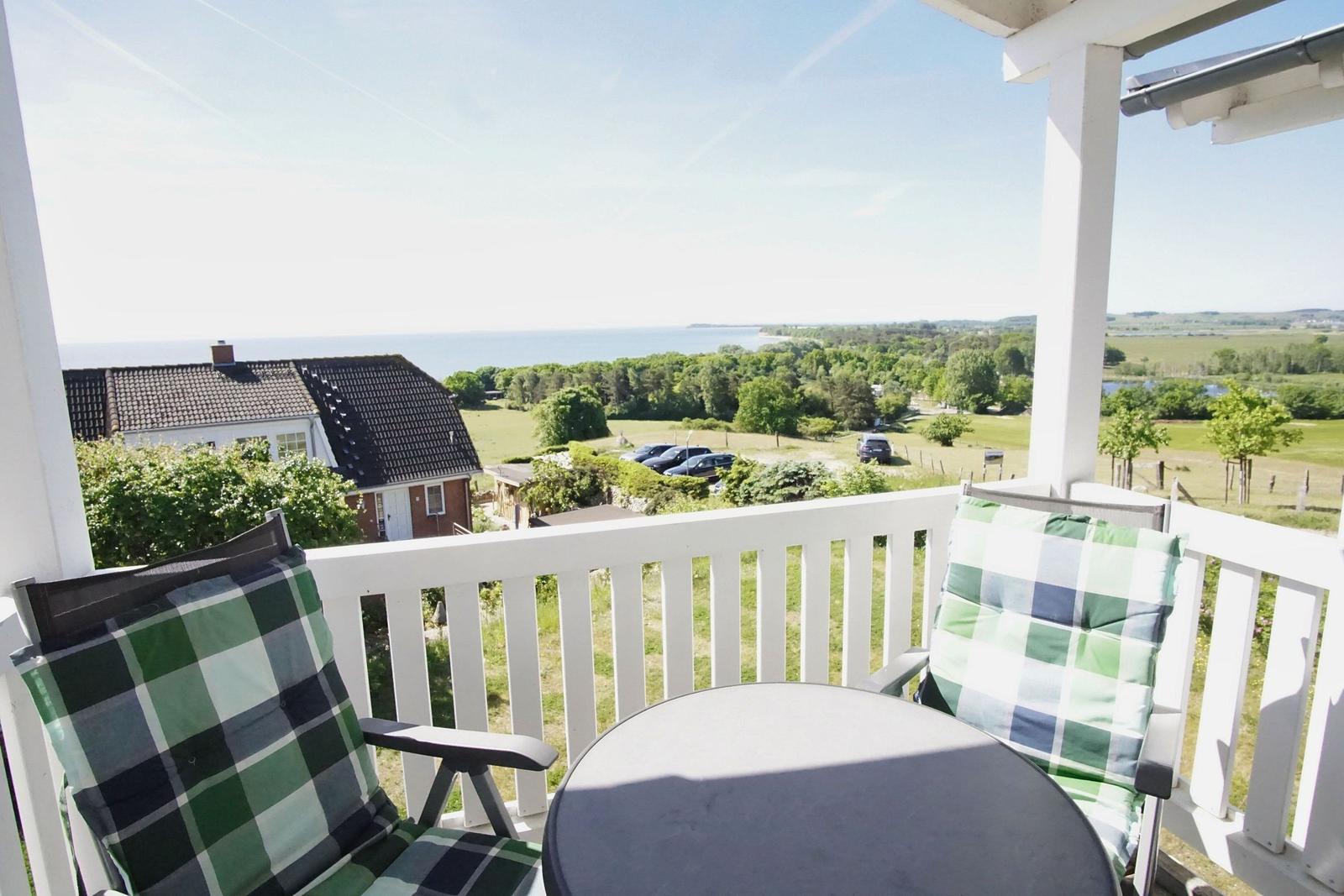 Terrasse mit Tisch und Stühlen, Blick auf Grünflächen und Meer.