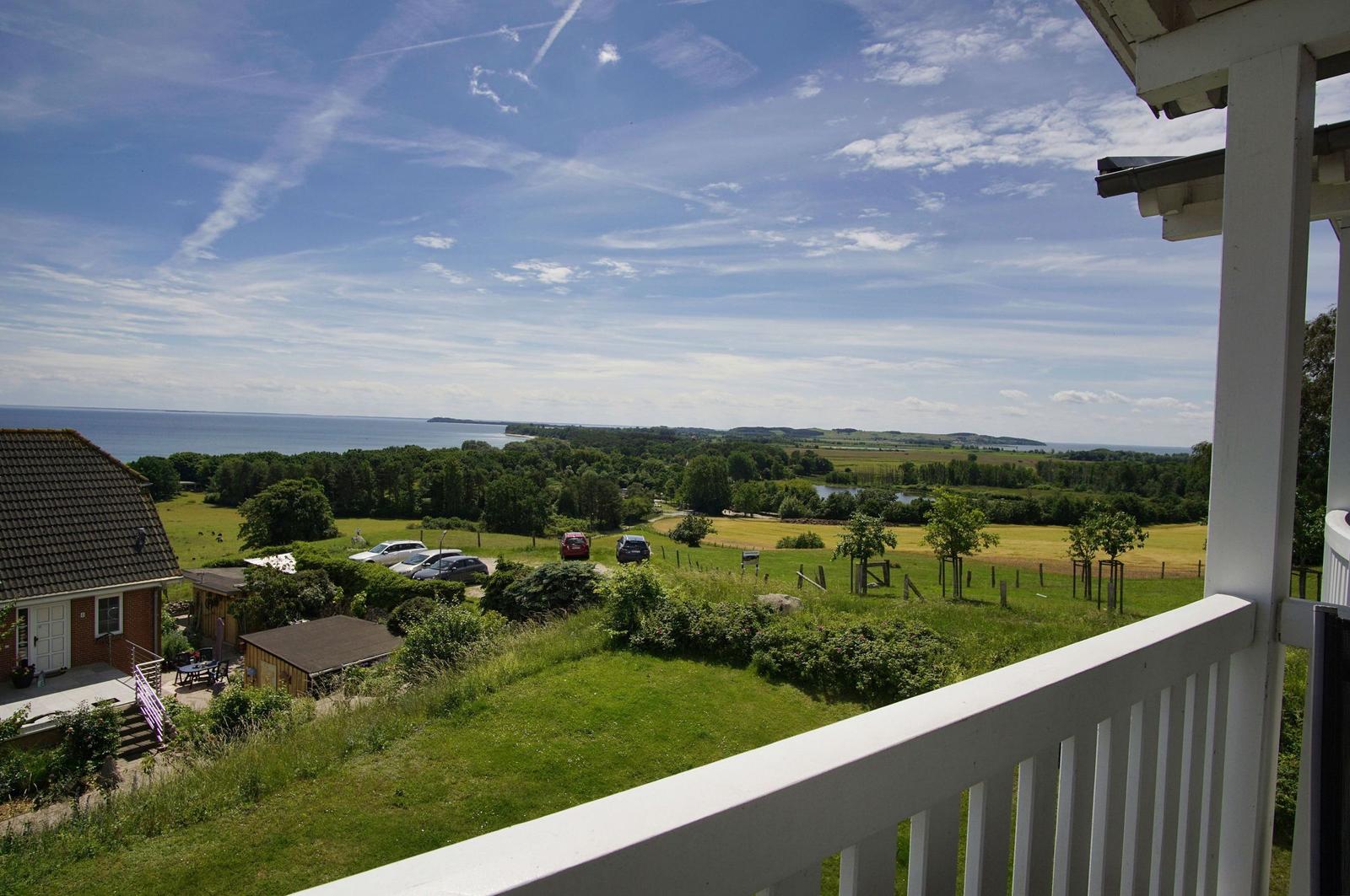 Weitläufiger Blick von Balkon auf Grünflächen, Bäume und Meer unter blauem Himmel.