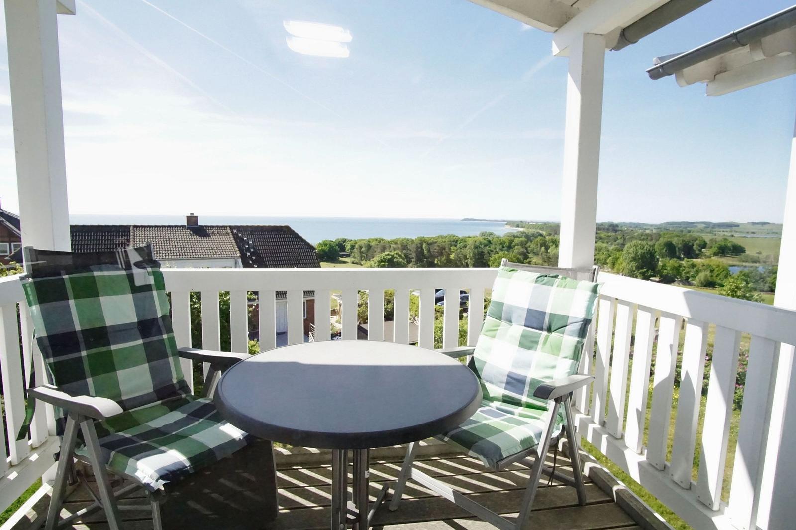 Terrasse mit Tisch und zwei Stühlen, Blick auf Meer und Landschaft.