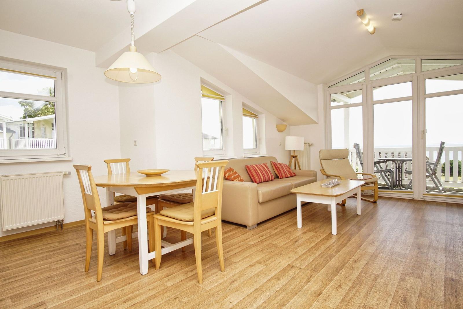 Wohn- und Essbereich mit Sofa, Tisch und Stühlen. Holzfußboden und große Fenster.
