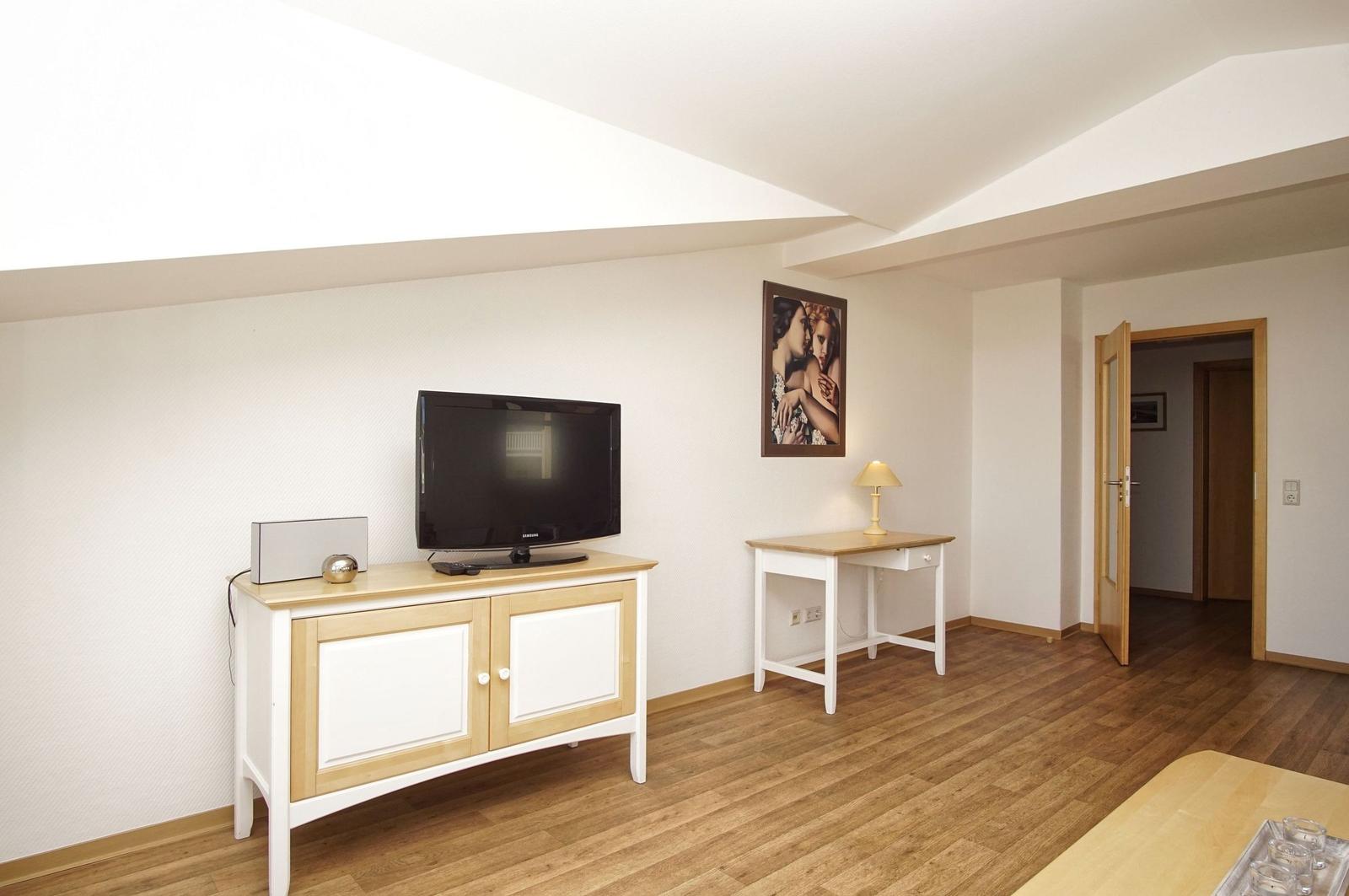 Wohnzimmer mit Fernseher, Schreibtisch und Holzboden.