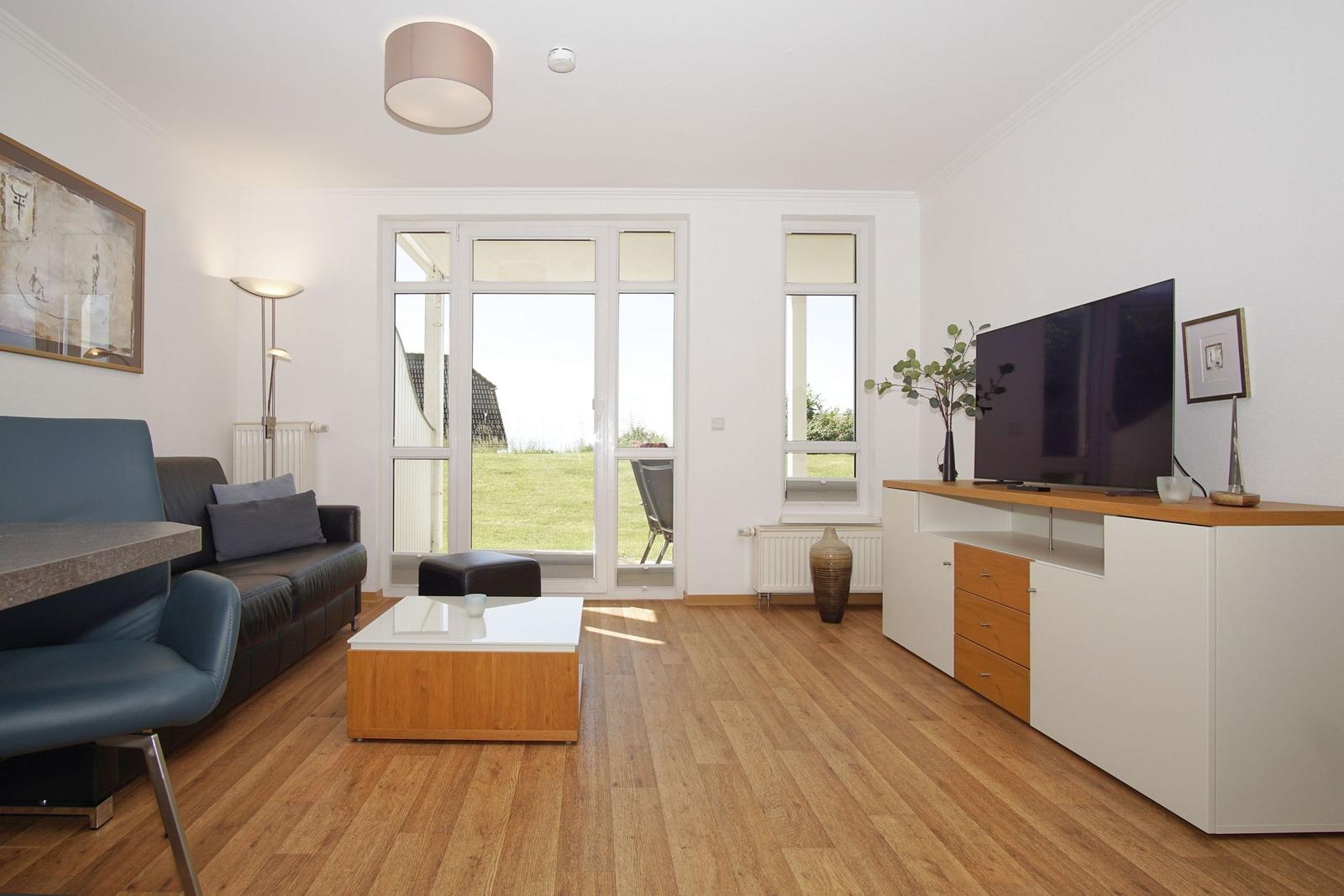 Living room with sofa, coffee table, and TV stand. Doorway to terrace with view of grass area.